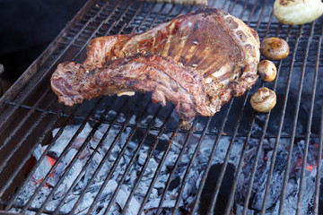 Meat and mushrooms are fried on the grill in a barbecue with flames. Ribs and champignons are fried over an open fire. Appetizing meal on the bbq. Grilled food. Picnic concept. Selective focus