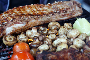 Meat, mushrooms and vegetables are fried on the grill in a barbecue with flames. Ribs, champignons, tomatoes and peppers are fried over an open fire. Appetizing meal on the bbq. Selective focus