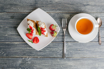 Honey cakes with strawberries and a cup of tea on a wooden background. Top view