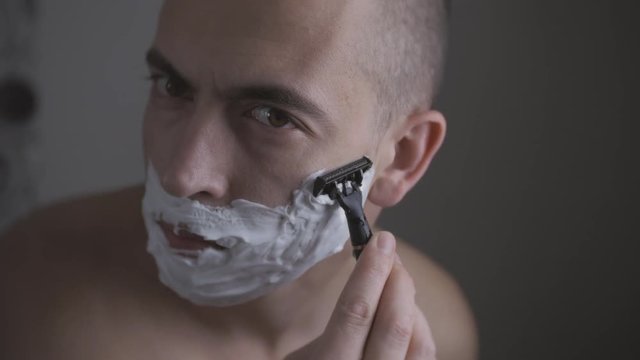 Man shaving with foam and manual razer. Close up of man shaving beard.
