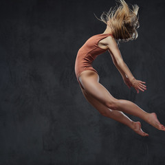 Young graceful ballerina dances and jumps in a studio. Isolated on a dark background.