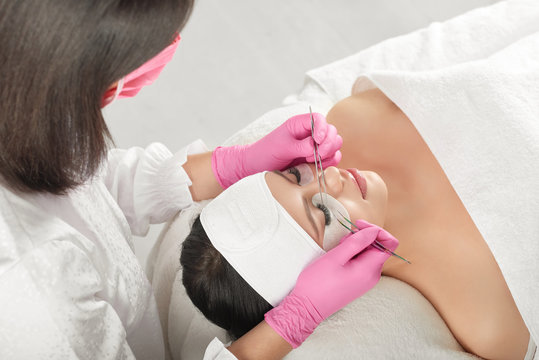 Lashes extension by professional lashmaker in beaty salon. Woman lying on cosmetologiacal coach during lashes enlarging. Model with pretty face wearing headbandage and stickers for lashmaking .