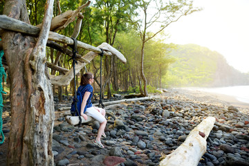 Young female tourist relaxing on a handmade swing on rocky beach of Pololu Valley on Big Island of Hawaii
