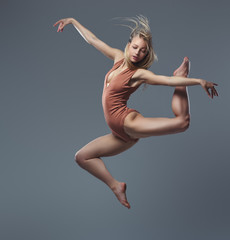 Fototapeta premium Young graceful ballerina dances and jumps in a studio. Isolated on a gray background.
