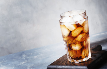 Alcoholic cocktail of rum-cola with ice, gray background, selective focus