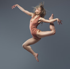 Young graceful ballerina dances and jumps in a studio. Isolated on a gray background. © Fxquadro