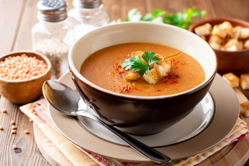 Red lentil cream soup with croutons in bowl on wooden table