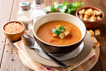 Red lentil cream soup with croutons in bowl on wooden table