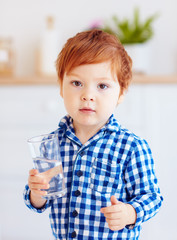 portrait of cute cute toddler baby boy drinking fresh water from glass early in the morning in pajamas