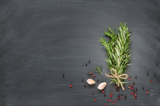 Bunch of rosemary with garlic and spices on chalk board