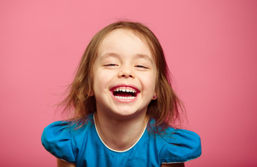 Frontal shot of laughter joyful little girl stands beside pink wall.