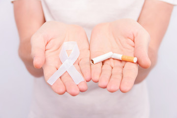 Oncological disease concept. Guy in white t-shirt holding white ribbon as symbol of lung cancer in one hand and broken cigarette in another.