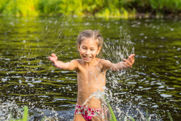 Adorable curly baby girl splashing in a beautiful river on a sunny summer day