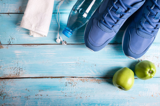 Flat lay sport shoes, bottle of water, apples, towel and earphones on blue background. Sport equipment. Healthy lifestyle, sport and diet concept. Copy space, top view
