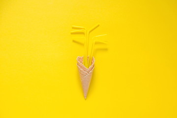 Ice cream cone with yellow drinking straws on a yellow background. Minimal food concept.