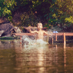 Young boy jumping, swimming and splashing in the river on summertime, image with square aspect ratio and warm toning