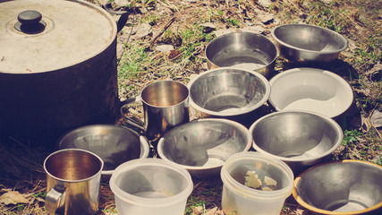 Clousep of cauldron and plates for soup standing on grass in forest, image with warm vintage toning