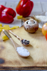 salt and pepper in wooden spoons surrounded by vegetables.