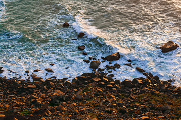 rocky shore and waves with foam. evening glare of sunlight on the water