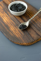 Fresh black caviar in a metal spoon on wooden board.