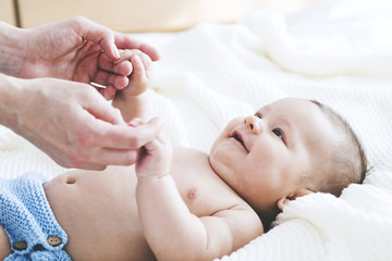 Close up of baby smiling at his mother. Newborn child looking up at mother and holding her hands....