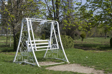 White swing in a green park. White wooden swing outdoor.