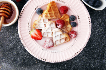 Traditional belgian waffles with fresh fruit and powder sugar on wooden board