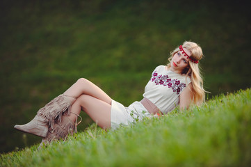 tender blonde woman sits on the grass dressed in a natural embroidered dress bandage on her head, on a green background stylish and cozy. The concept of advertising the love of nature. place for text