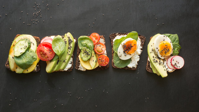 Different sandwiches with vegetables, eggs, avocado, tomato, rye bread on black chalkboard background. Top vew. Appetizer for party. Flat lay.