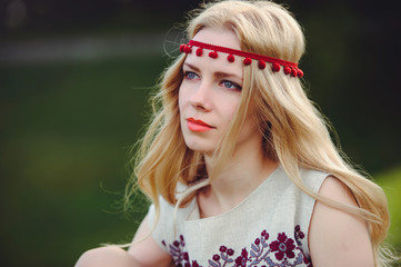 tender blonde woman sits on the grass dressed in a natural embroidered dress bandage on her head, on a green background stylish and cozy. The concept of advertising the love of nature. place for text