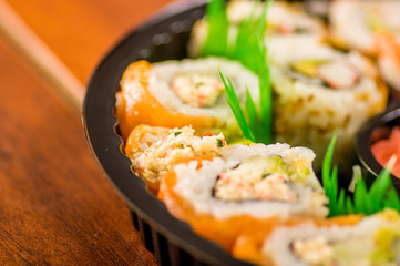 Close up of selective focus of large set of japanese rolls on a black plastic plate over a wooden table