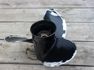 Damaged black aluminum propeller boat motor with curved blades on the background of gray boards