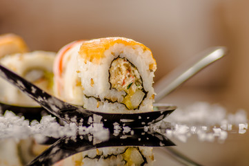 Close up of selective focus of delicious sushi rolls over a metallic spoon with small grains of salt served on black table