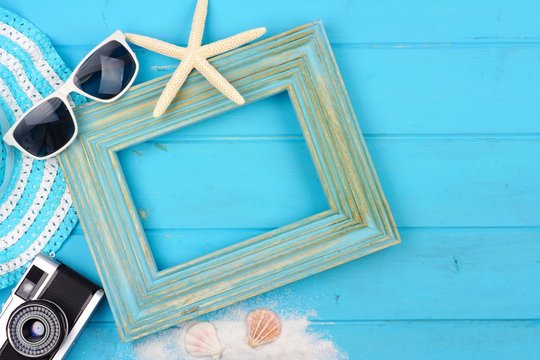 Beach travel concept mock up with frame and surrounding accessories on a blue wood background. Flat lay with copy space.