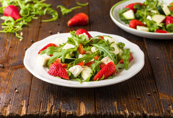 Fresh vegetable strawberry salad on white plate on natural rustic desk.