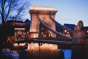 Obraz premium Night view of a famous Budapest Szechenyi Chain Bridge, a suspension bridge that spans the River Danube between Buda and Pest, the western and eastern sides of Budapest