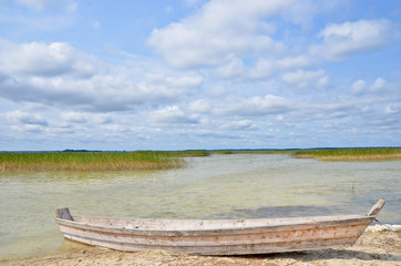 Obraz premium Wooden fishing boat on the lake beach with blue sky, yellow sand and transparent water