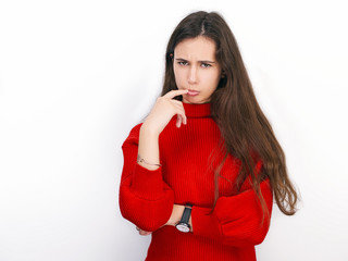 Young beautiful brunette woman in red sweater showing suspicious emotion posing against white background