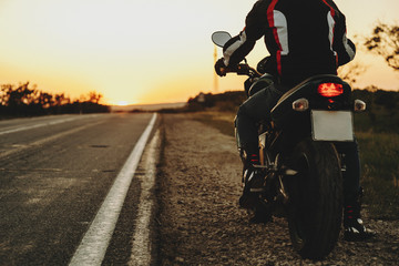 Back view crop of a motorcyclist traveler starting his road after resting against sunset.