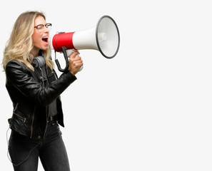 Young student woman with headphones communicates shouting loud holding a megaphone, expressing...