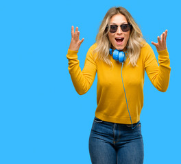 Young beautiful woman with headphones happy and surprised cheering expressing wow gesture