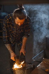 Blacksmith  works as a hand hammer with molten metal on the anvil in the smithy with a spark firework.