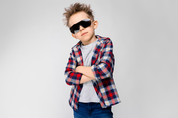 A handsome boy in a plaid shirt, gray shirt and jeans stands on a gray background. The boy in the...