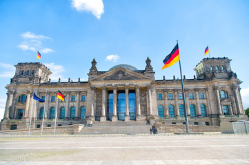 Naklejka premium German flags waving in the wind at famous Reichstag building, seat of the German Parliament (Deutscher Bundestag), on a sunny day with blue sky and clouds, central Berlin Mitte district, Germany
