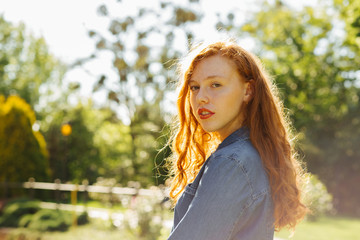 Street portrait of elegant red haired young model posing in sun glare. Empty space