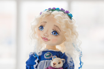 Portrait of textile handmade vintage doll with blue eyes, long blond hair in old blue textile dress with gentle print, in white shirt with purple boots on white background. She holding little textile