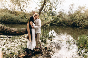 A beautiful couple in the boo style embraces sitting on a branch over the lake