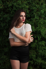 Naklejka premium Amazing brunette girl in trendy shirt posing on a green thuja background