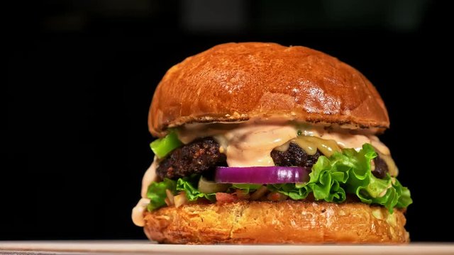 Cool beautiful fresh juicy cooked burger rotate on turntable. Very luscious air bun and marbled beef. Restaurant where each burgers is cooked by hand. Not made ideal. Not conveyor. Looks real, loving