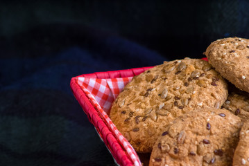 homemade oat cookies with sunflower seeds in and near red checkered basket on dark blue background